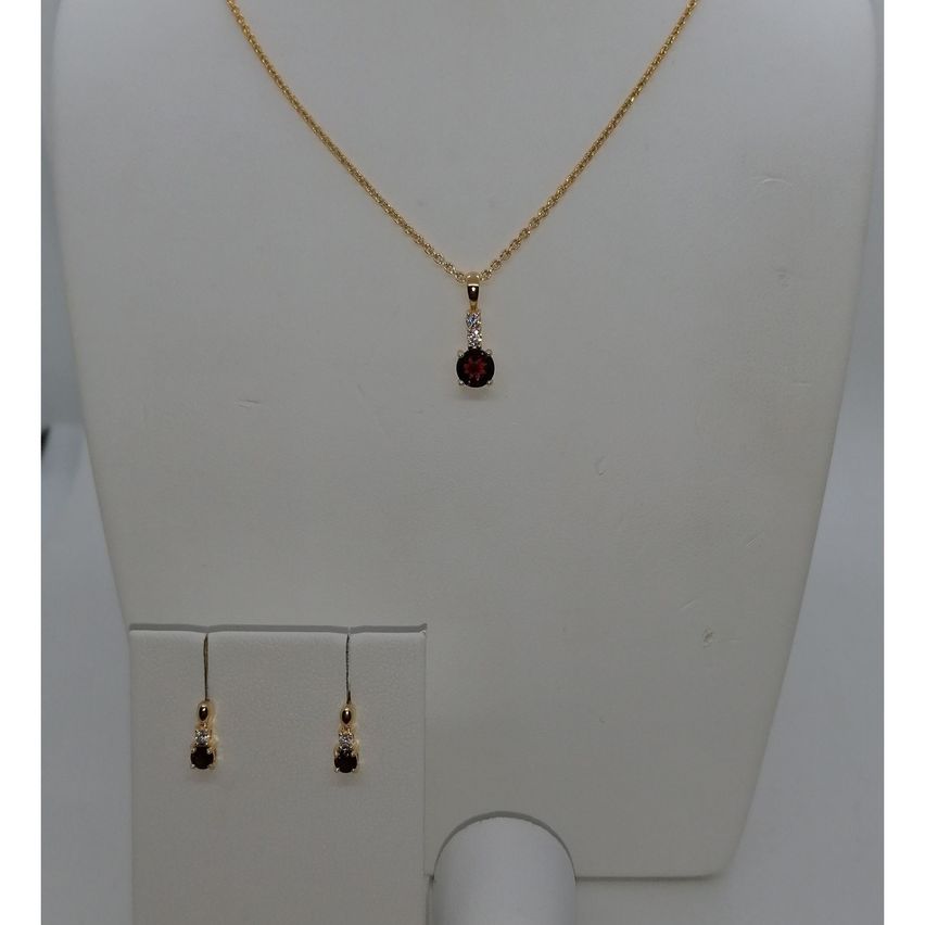 Eine goldene Halskette mit einem roten Steinanhänger, begleitet von passenden Ohrringen, auf einem weißen Mannequin ausgestellt.