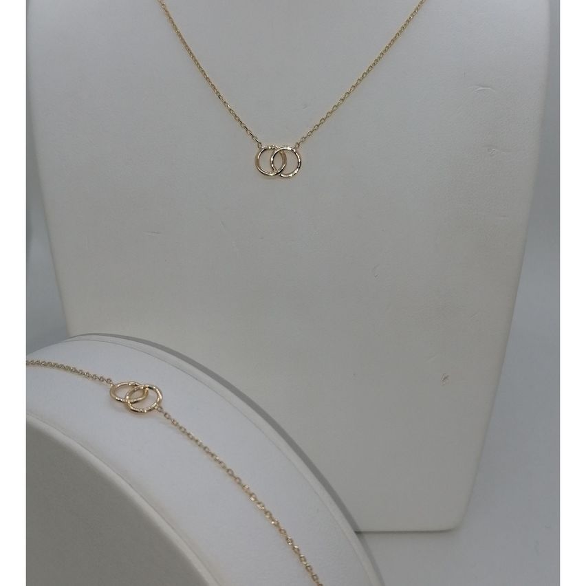 Eine goldene Halskette mit zwei ineinander verschlungenen Ringen, ausgestellt auf einem Mannequin. Ein ähnliches Design befindet sich auf einem Armband darunter.