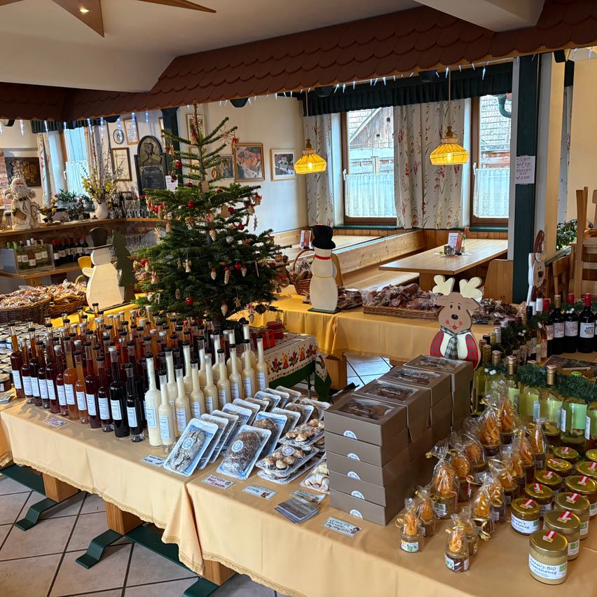 Ein Raum mit Weihnachtsdekoration, der einen Tisch mit Flaschen Wein, Flaschen Sirup und verschiedenen Schachteln mit Süßigkeiten, einem Weihnachtsbaum und anderen Feiertagsartikeln zeigt.