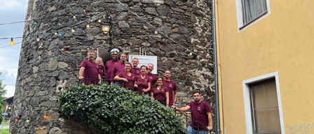 Eine Gruppe von Menschen in Purpurhemden posiert vor einem alten Steingebäude, mit einem Schild, das darauf hinweist, dass es sich um ein Stadtmuseum handelt.