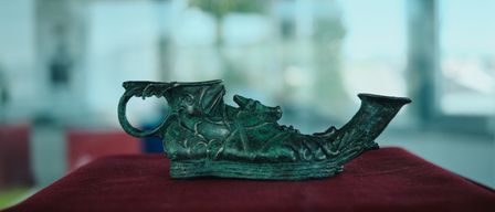 Ein grünes Keramikobjekt mit kunstvollen Drachendesigns ruht auf einem roten Tuch. Das Objekt scheint ein antikes Stück zu sein, das möglicherweise als Dekorationsgegenstand verwendet wurde.