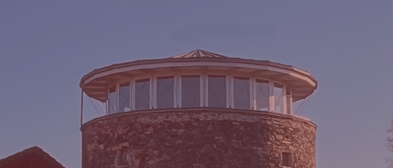 Ein kreisförmiges Gebäude mit steinernem Äußeren, mit mehreren Fenstern und einem kuppelförmigen Dach. Die Fenster sind in einer Reihe angeordnet, durch weiße Rahmen getrennt.