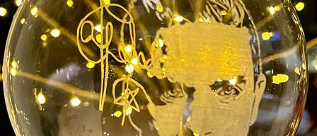 Eine Glaskugel mit einer goldenen Silhouette eines Männergesichts, mit einer Unterschrift, beleuchtet von gelben Lichtern im Hintergrund.