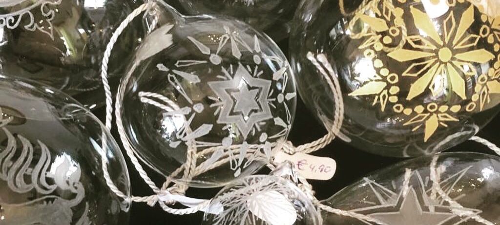 Eine Sammlung handgefertigter Glas-Weihnachtskugeln mit einzigartigen Designs. Jede Kugel ist sorgfältig mit filigranen Mustern und Goldblattdetails verziert. Vor dunklem Hintergrund präsentiert.