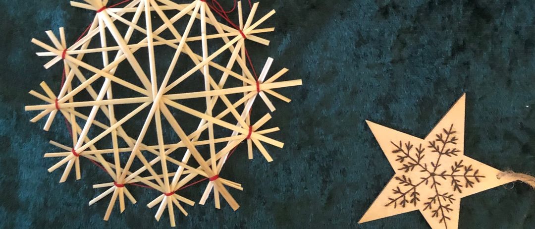 Mehrere Holzschneeflocken hängen an einem dunkelblauen Tuch. Sie sind mit roten Fäden verbunden. Ein goldener Stern befindet sich neben ihnen.