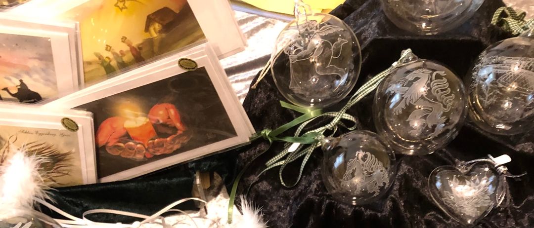 Eine Sammlung von kunstvoll gestalteten Glaskugeln auf einem grünen Samttuch, mit verschiedenen Designs wie Schneeflocken, Herzen und einem Schneemann. Einige hängen, während andere auf schwarzem Samt ausgestellt sind.