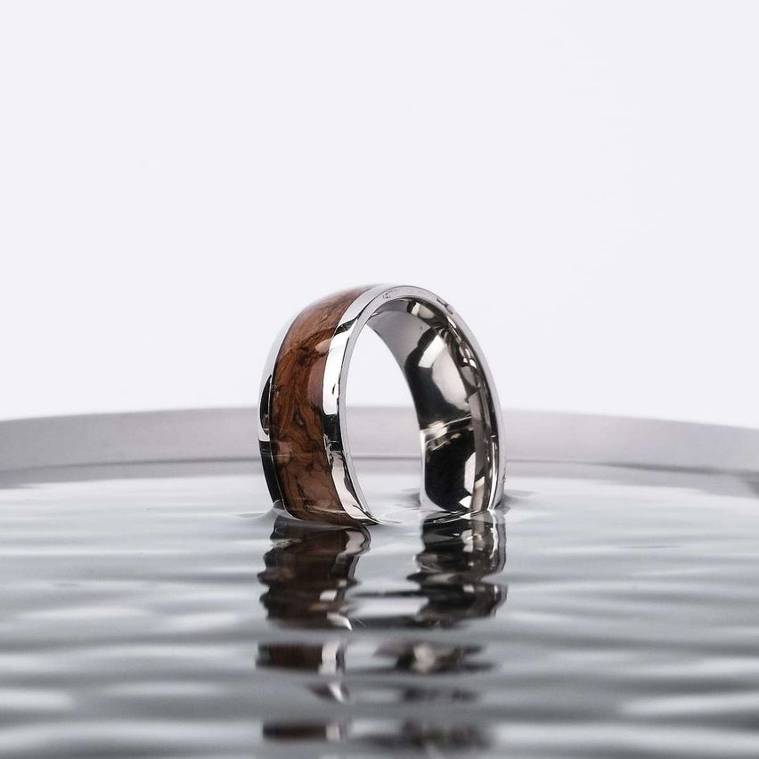 Ein Silberring mit hölzerne Einlage sitzt im Wasser und reflektiert Licht.