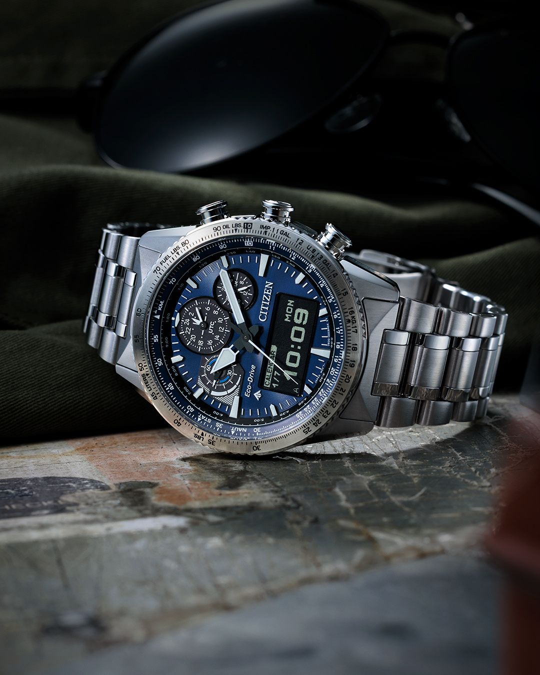 Eine silberne Armbanduhr mit blauem Zifferblatt wird auf einer rauen Oberfläche gezeigt, die Zeit 10:08 anzeigend. Die Uhr hat ein digitales Display und verschiedene Unterzifferblätter.