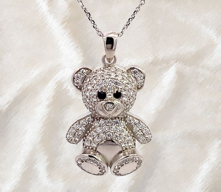 Eine Silberkette mit einem diamantbesetzten Teddybären-Anhänger, der auf einer weißen Oberfläche ruht.