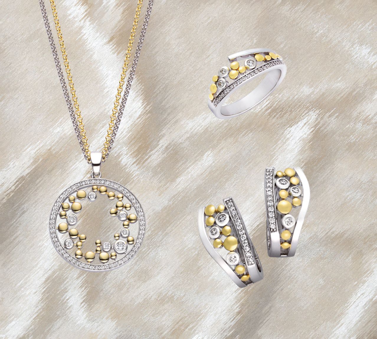 Vier Schmuckstücke, darunter eine Halskette, ein Ring und ein Paar Ohrringe, sind auf einer strukturierten Oberfläche zu sehen. Die Halskette ist kreisförmig mit einem Gold- und Silberfarbschema. Der Ring und die Ohrringe sind silbern mit gelben und weißen Steinen.