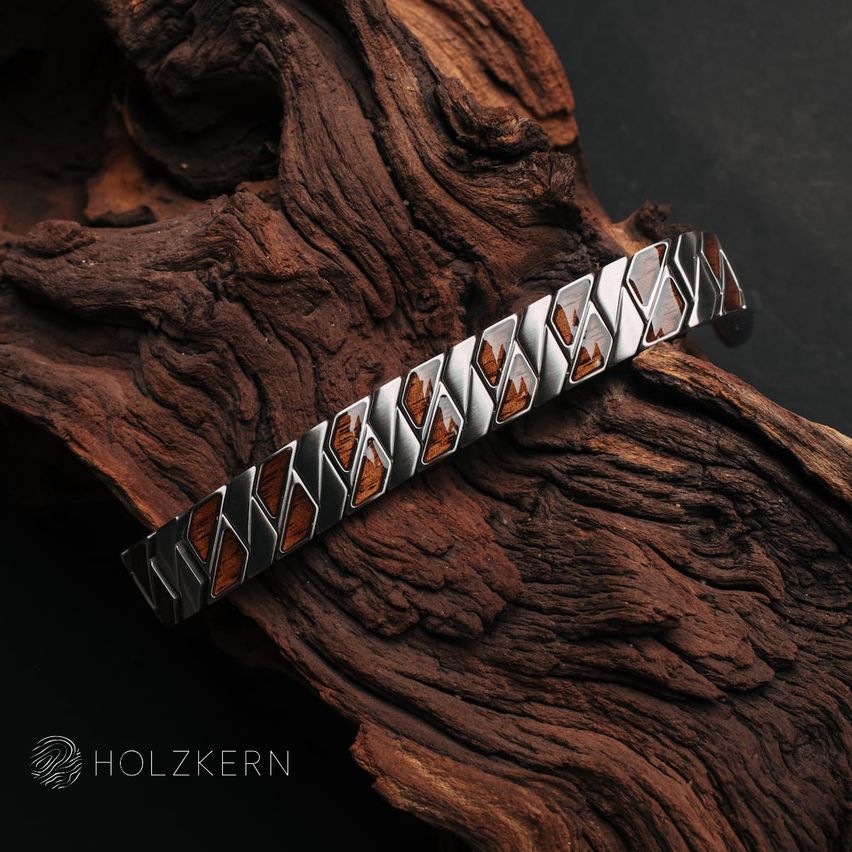 Eine silberne Armband mit dreieckigen Holzeinlagen, auf einer strukturierten Holzoberfläche platziert, mit dem Markennamen 'Holzkern'.