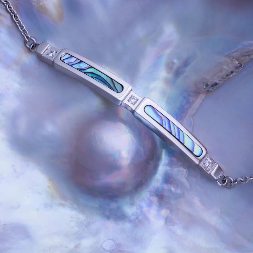 Eine Silberarmband mit blauen und grünen Perlmutteinlagen wird auf einer Perlmuschel ausgestellt.