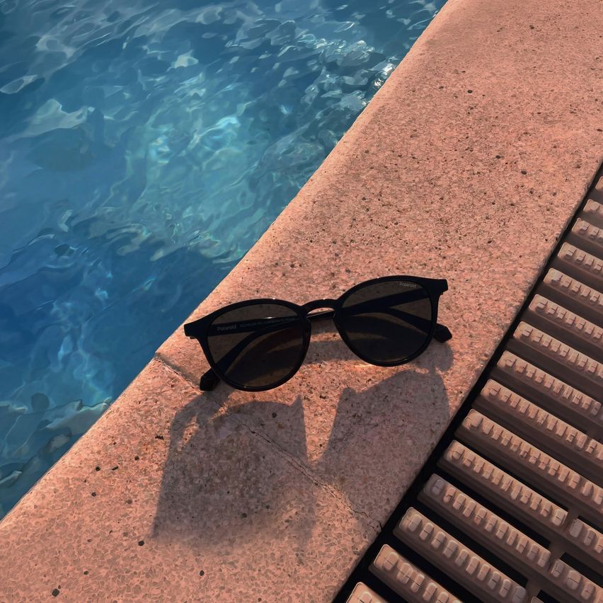 Schwarze Sonnenbrille mit Polaroid-Logo liegt am Rand eines Pools. Das Wasser ist klar und blau.