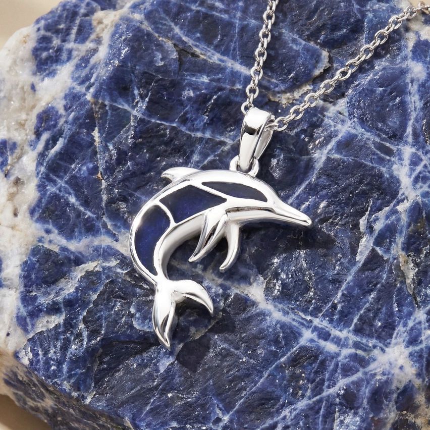 Ein silberner Delfin-Anhänger liegt auf einem blauen Stein und zeigt sein schlankes Design und seine detaillierten Merkmale.