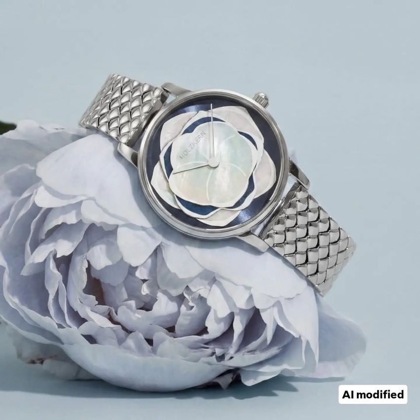 Eine silberne Uhr mit einem weißen Blumendesign auf dem Zifferblatt liegt auf einer großen weißen Blume vor blauem Hintergrund.