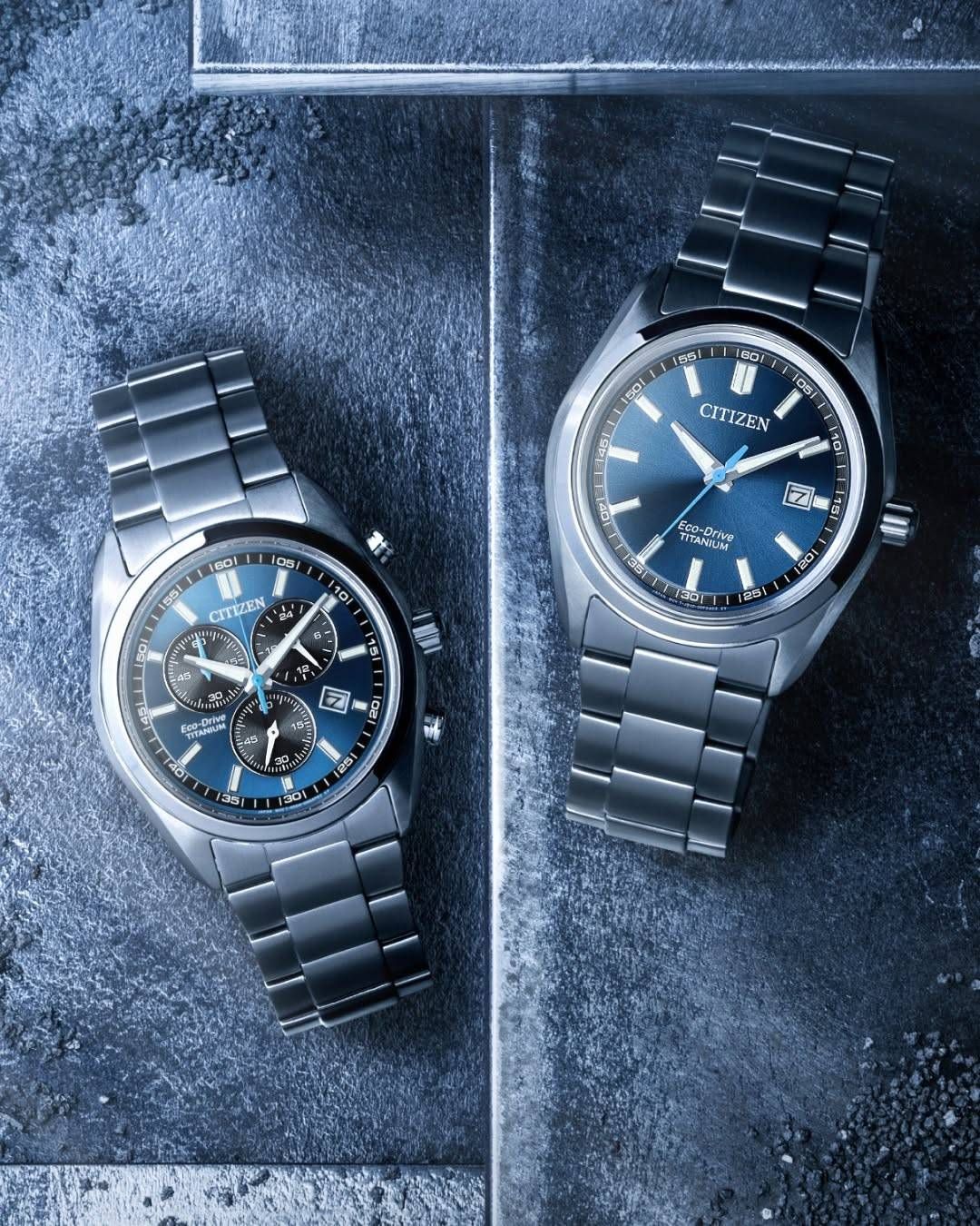 Zwei silberne Citizen-Uhren mit blauen Zifferblättern auf dunklem Hintergrund. Die linke Uhr hat 'CITIZEN' auf dem Zifferblatt. Die rechte Uhr zeigt 'CITIZEN' und 'Eco-Drive Titanium'. Beide haben blaue Zeiger und digitale Markierungen.