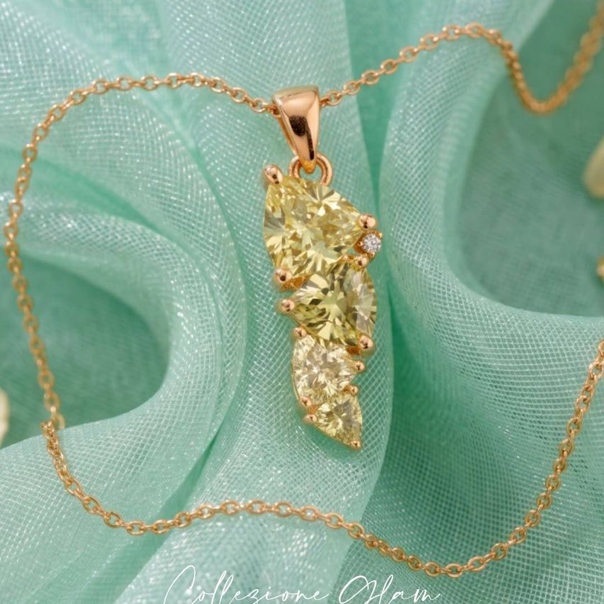 Eine goldene Halskette mit einem Anhänger aus drei gelben Edelsteinen, auf einem mintgrünen Stoff.