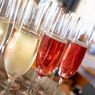 Several wine glasses filled with different colored wines sit on a table. The glasses are lined up. The liquid reflects light.