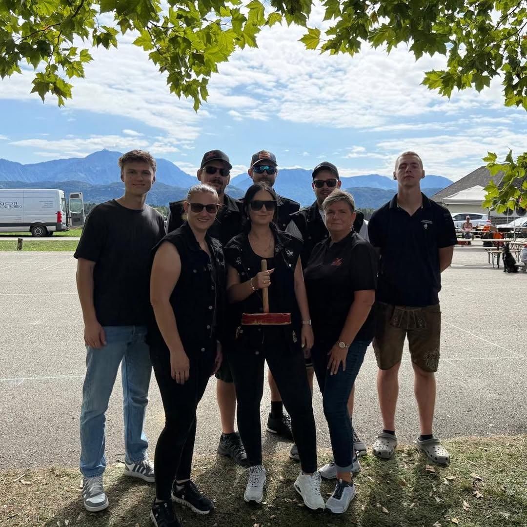 Eine Gruppe von Menschen in Freizeitkleidung posiert für ein Foto auf einem Parkplatz mit Bergen im Hintergrund.