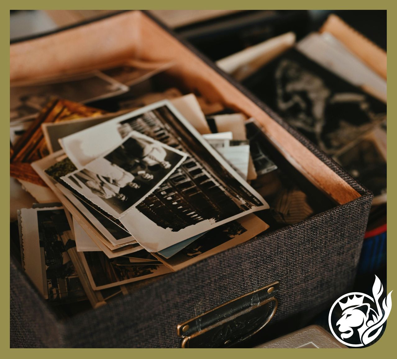 Ein hölzerner Kasten gefüllt mit alten Schwarz-Weiß-Fotos, einige mit Menschen, einem Gebäude und einem Löwenkopf-Logo in der Ecke.