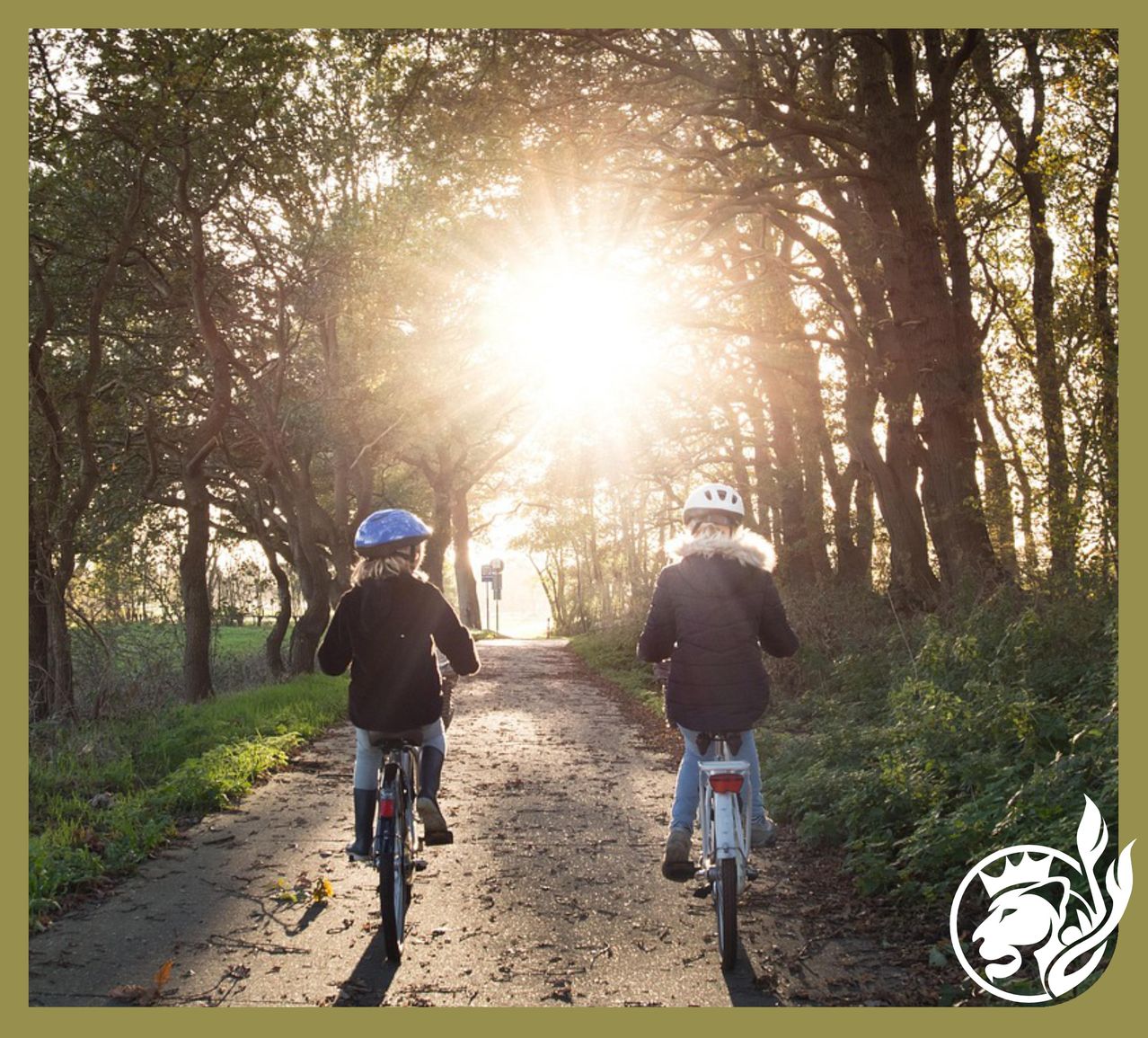 Zwei Kinder fahren auf einem Feldweg mit Bäumen an beiden Seiten. Die Sonne scheint hell im Hintergrund.