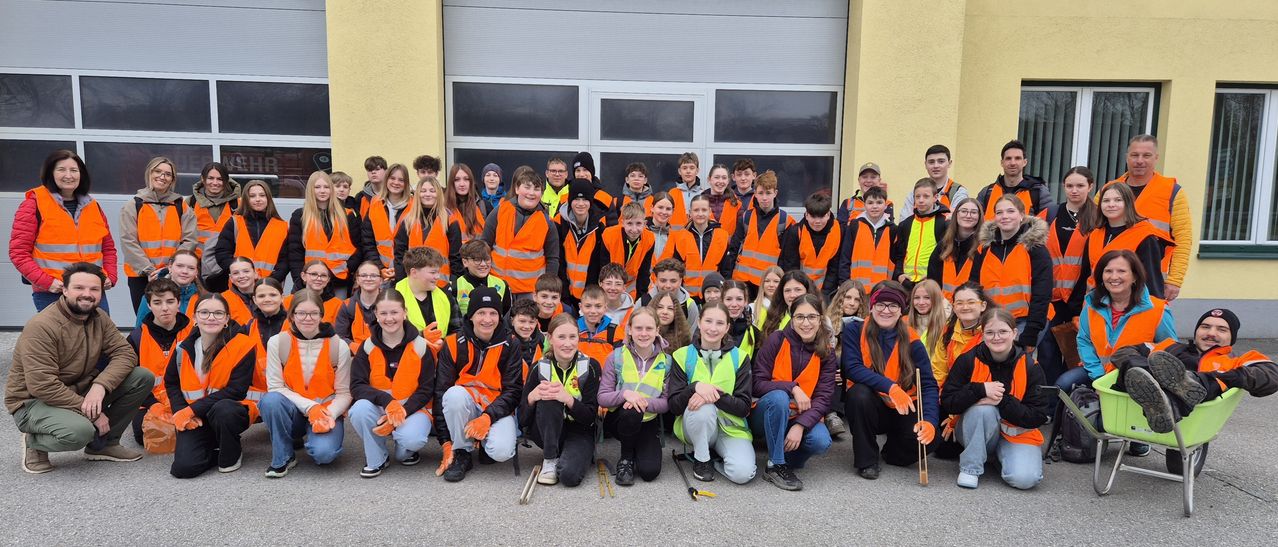 A group of students in safety vests pose for a photo outside a building with glass doors.