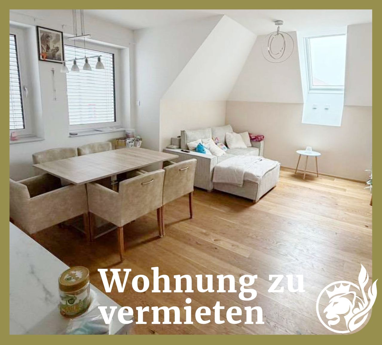 Ein heller Wohnbereich mit Holzboden, Esstisch, Couch und Fenstern. Ein gerahmtes Bild befindet sich an der Wand über der Couch. Der Raum hat einen Dachboden mit einem Bett und einer runden Lampe.