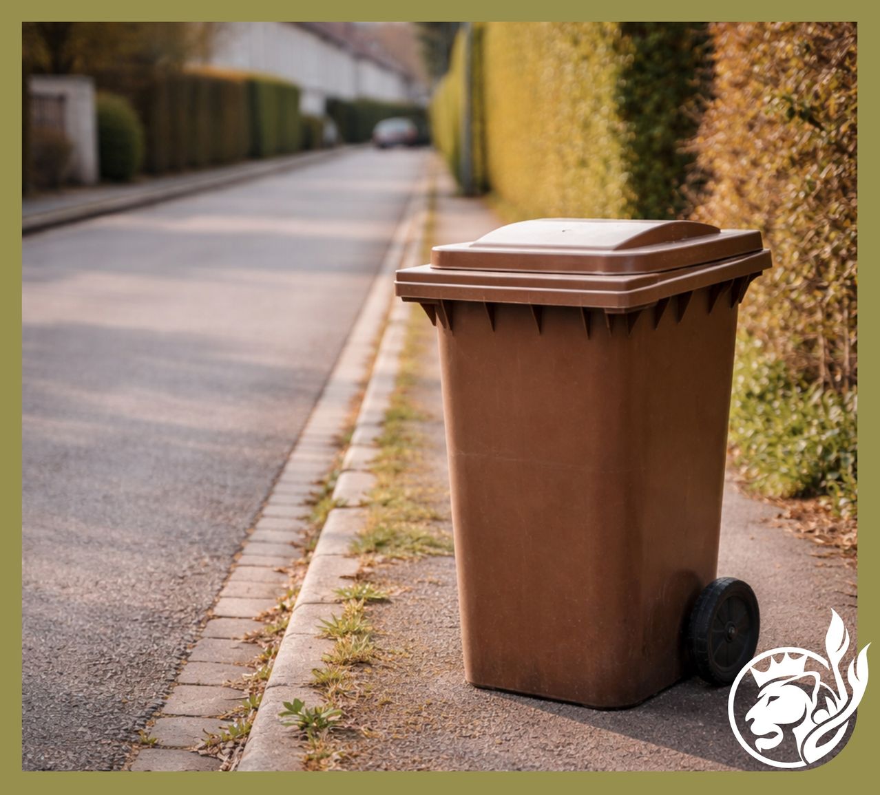 Ein brauner Mülleimer mit Rädern steht auf dem Bürgersteig neben einer asphaltierten Straße, mit Büschen und einem Auto in der Ferne.