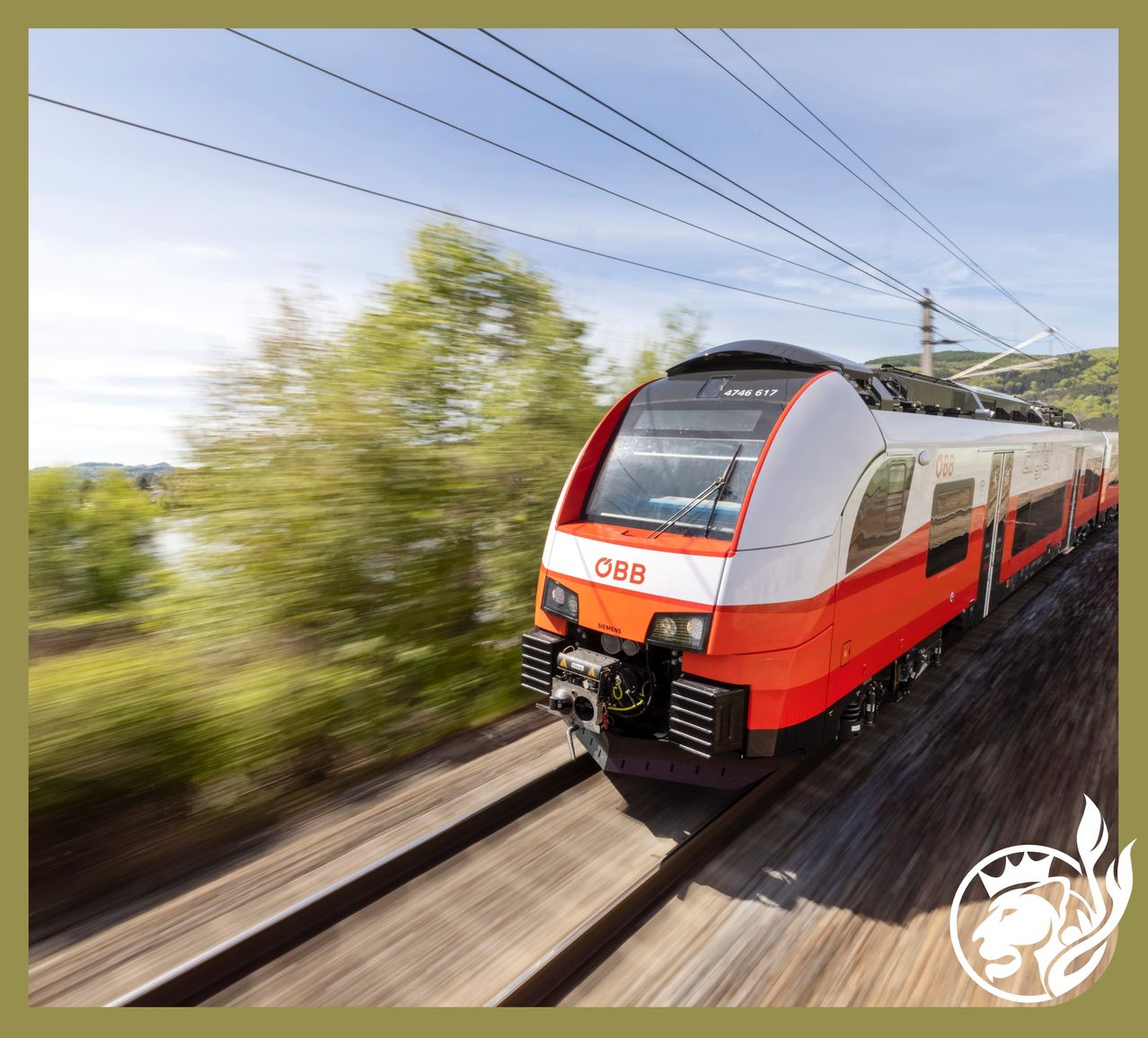 Ein moderner, weißer und orangefarbener Zug mit dem Wort OBB auf der Vorderseite fährt auf den Gleisen. Im Hintergrund sind Bäume und Berge zu sehen.