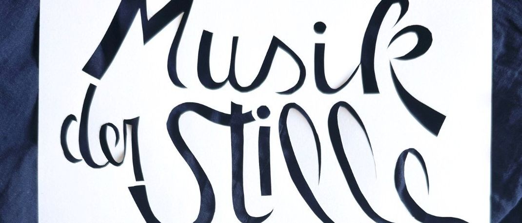 Ein weißes Blatt mit schwarzem Text, der 'Musik der Stille' über einem Wassertropfen liest. Das Kunstwerk befindet sich auf einem blauen Hintergrund.