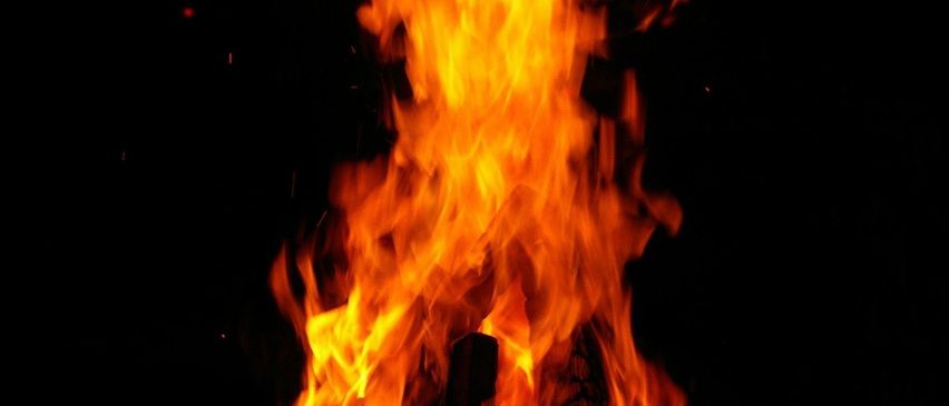 Ein Lagerfeuer brennt bei Nacht hell und beleuchtet die Flammen mit einem dunklen Hintergrund.