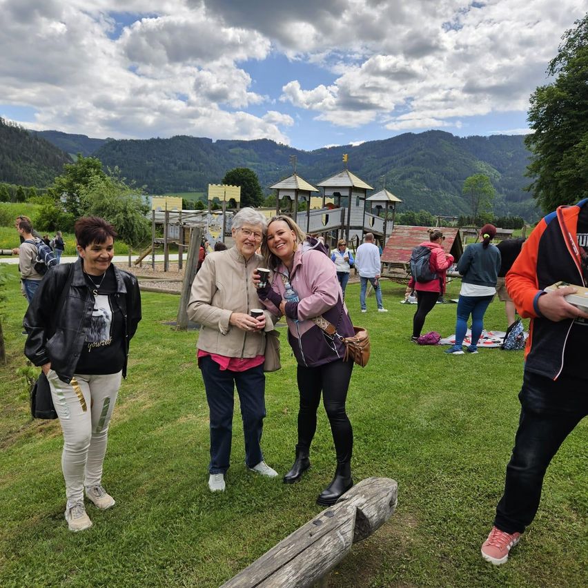 Vier Frauen und ein Mann stehen auf einem Rasenfeld mit Bergen im Hintergrund. Eine Frau hält einen Becher und andere lächeln.