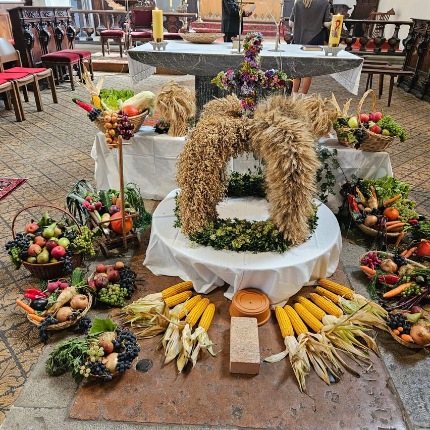 Ein Altar in einer Kirche ist mit verschiedenen Früchten, Gemüse und Getreide geschmückt. Im Mittelpunkt steht eine Weizengirlande. Körbe mit Obst und Gemüse umgeben den Altar.