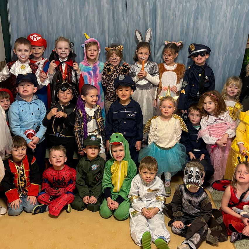 Eine Gruppe von Kindern in verschiedenen Kostümen, darunter ein Pirat, ein Hase, ein Einhorn, ein Polizist und ein Superheld, posiert für ein Foto.