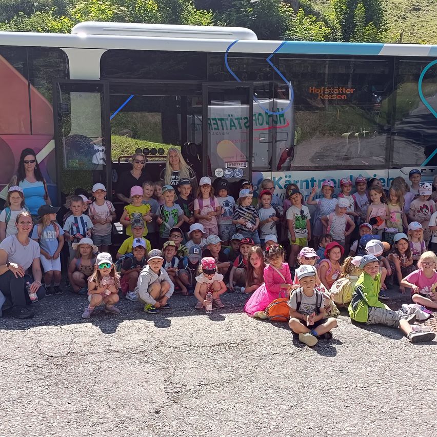 Eine Gruppe von Kindern und Erwachsenen posiert für ein Foto vor einem Bus mit fremdsprachigem Text.