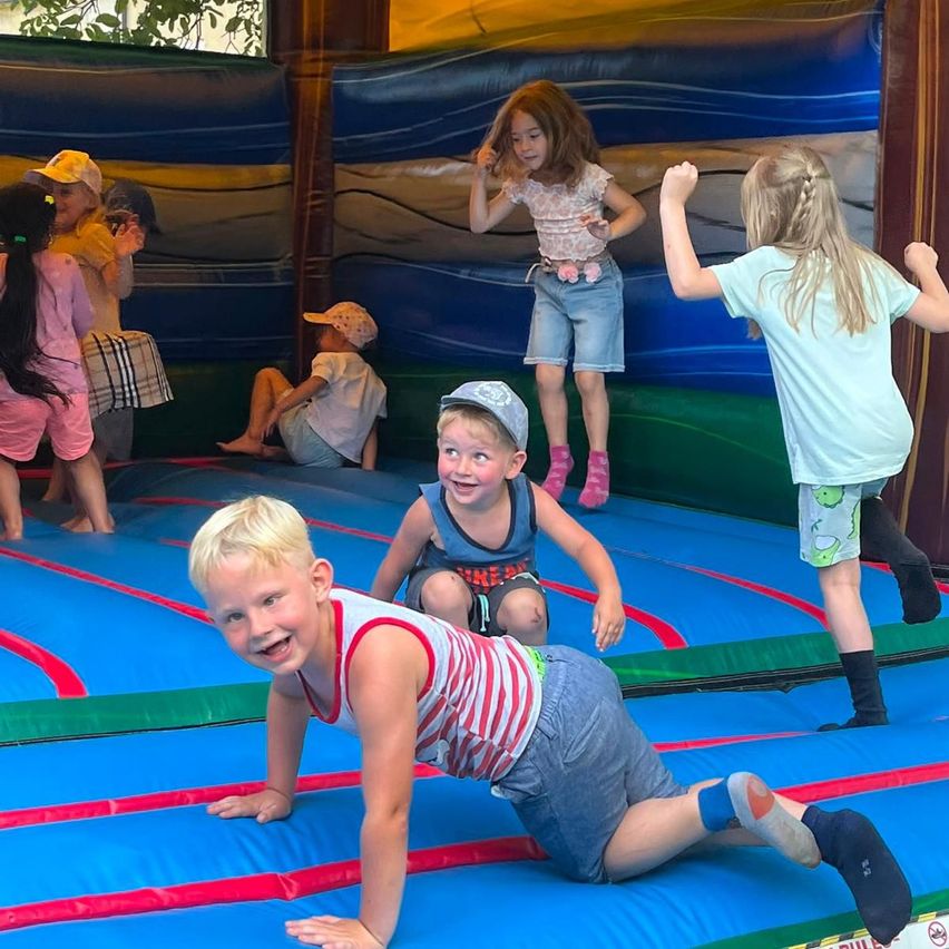 Eine Gruppe junger Kinder spielt in einem bunten aufblasbaren Sprunghaus. Einige springen, während andere zusehen.