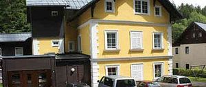 Ein großes gelbes Gebäude mit mehreren Fenstern und einem braunen Mittelteil, vor dem zwei Autos geparkt sind.