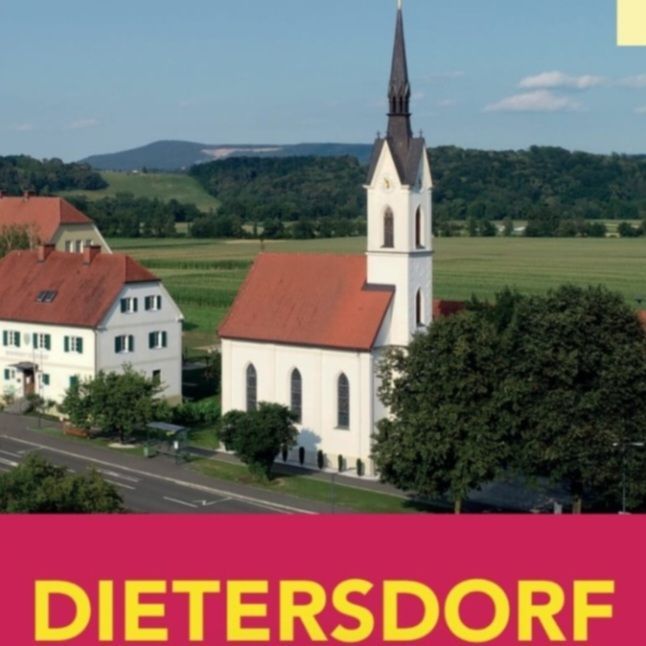 Ein Luftbild von Dietersdorf mit einer weißen Kirche mit Turm, umgeben von grünen Feldern und Bäumen, mit einem gelben Schild darüber.
