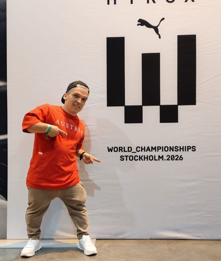 Ein Mann in einem roten T-Shirt mit der Aufschrift Osterreich posiert vor einem Banner der Weltmeisterschaften.