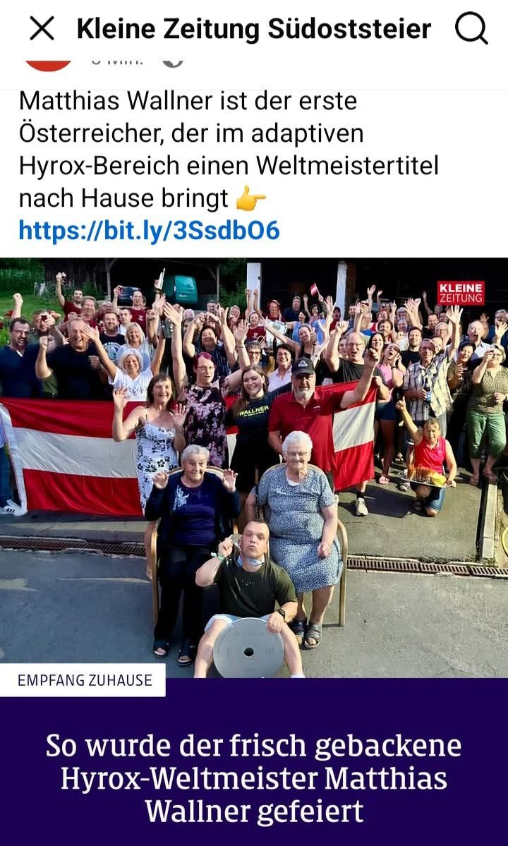 Eine Gruppe von Menschen steht und sitzt draußen, eine Schweizer Flagge wehend. Einige halten Getränke, und zwei ältere Frauen sitzen in Stühlen. Ein Mann hält eine große Medaille. Ein rot-weißes Schild ist rechts.