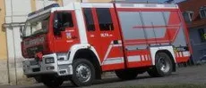 Ein roter Feuerwehrwagen steht vor einem gelb-weißen Kirchengebäude mit blauem Himmel im Hintergrund.