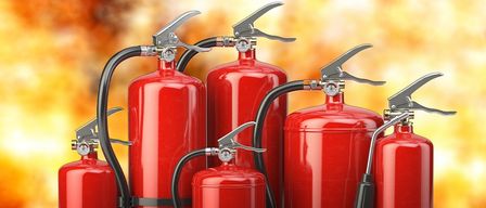 Eine Reihe von sechs roten Feuerlöschern vor einem feuerroten Hintergrund. Jeder Löscher hat einen silbernen Griff und einen schwarzen Schlauch.