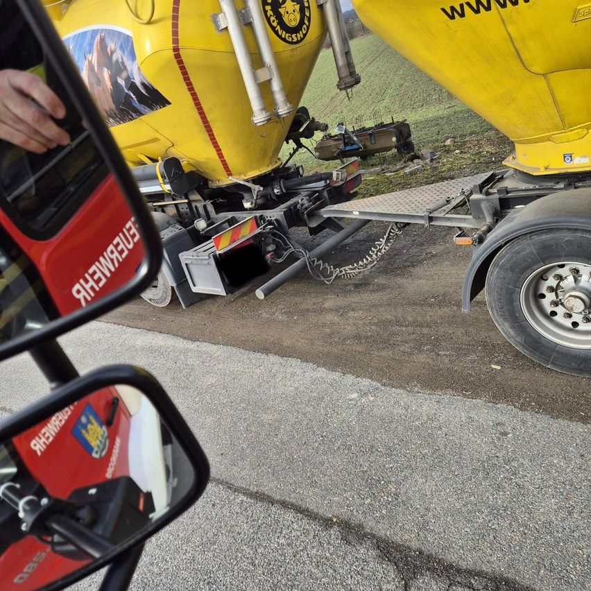 Ein Rückspiegel eines Fahrzeugs zeigt einen großen gelben Anhänger mit rotem Streifen und der Aufschrift 'www'. Der Anhänger ist auf einer Straße geparkt.