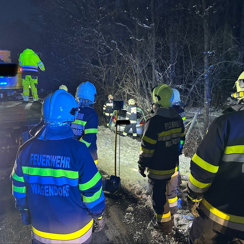 Feuerwehrleute in Schutzkleidung sind am Unfallort eines Fahrzeugs. Eine Person erhält Pflege.
