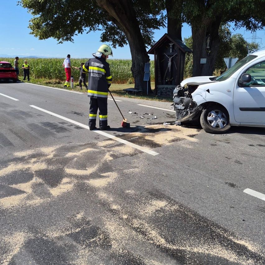 Ein Feuerwehrmann reinigt Trümmer von einem Verkehrsunfall mit einem weißen Van. In der Nähe sind eine kleine Kapelle und ein Maisfeld zu sehen.