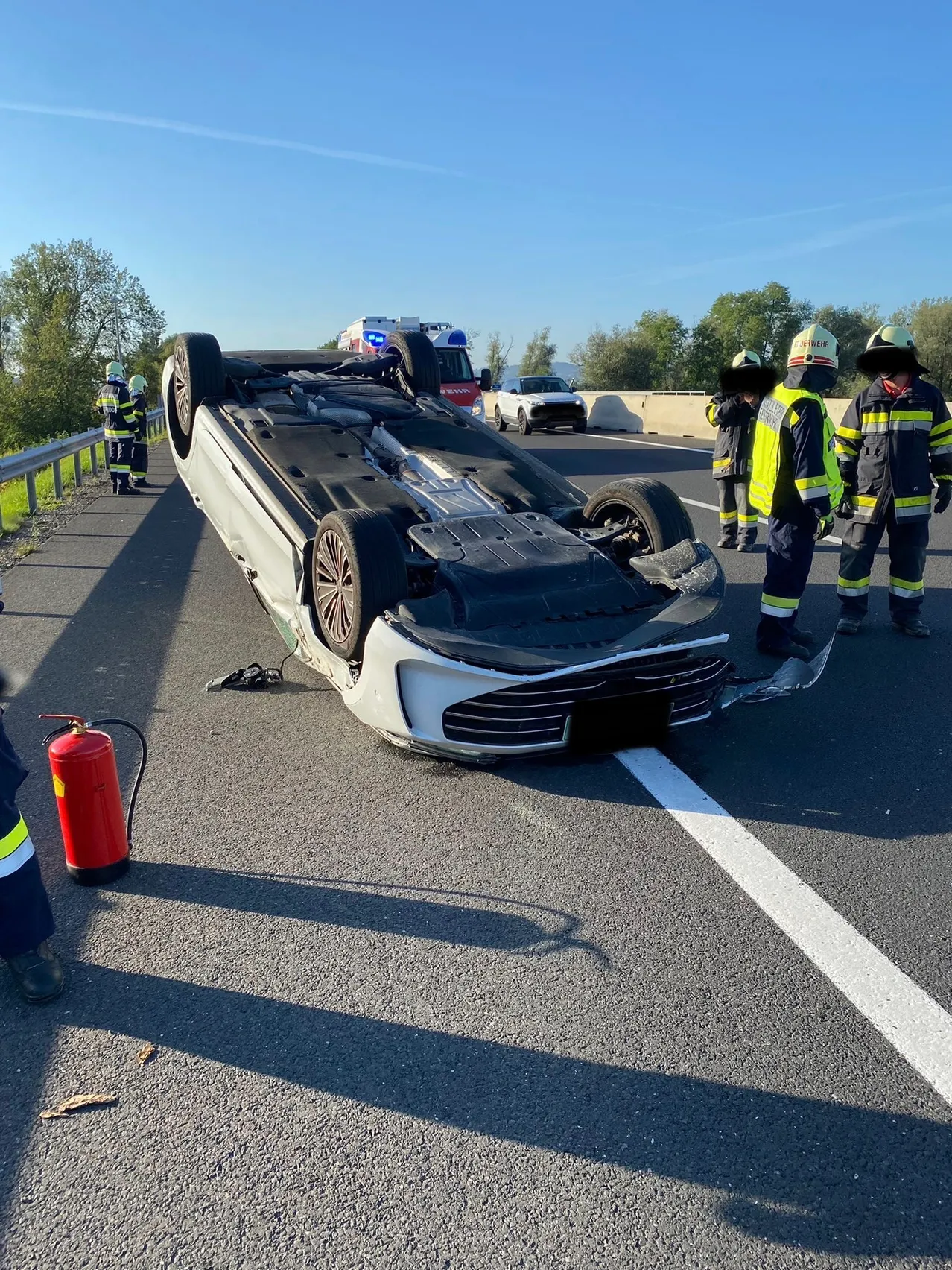 Ein weißer Wagen ist auf einer Autobahn umgekippt, und Rettungskräfte sind am Unfallort.