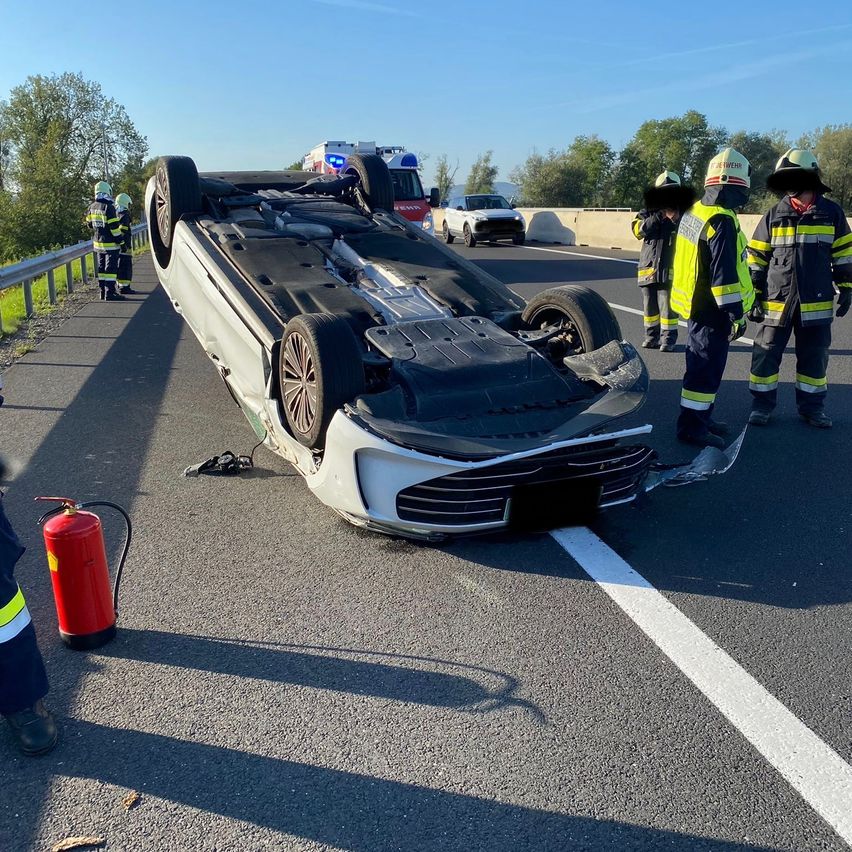 Ein weißer Wagen ist auf einer Autobahn umgekippt, und Rettungskräfte sind am Unfallort.