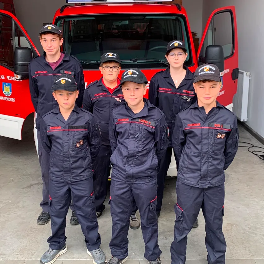 Eine Gruppe junger Feuerwehrleute in Uniform vor einem roten Feuerwehrauto.