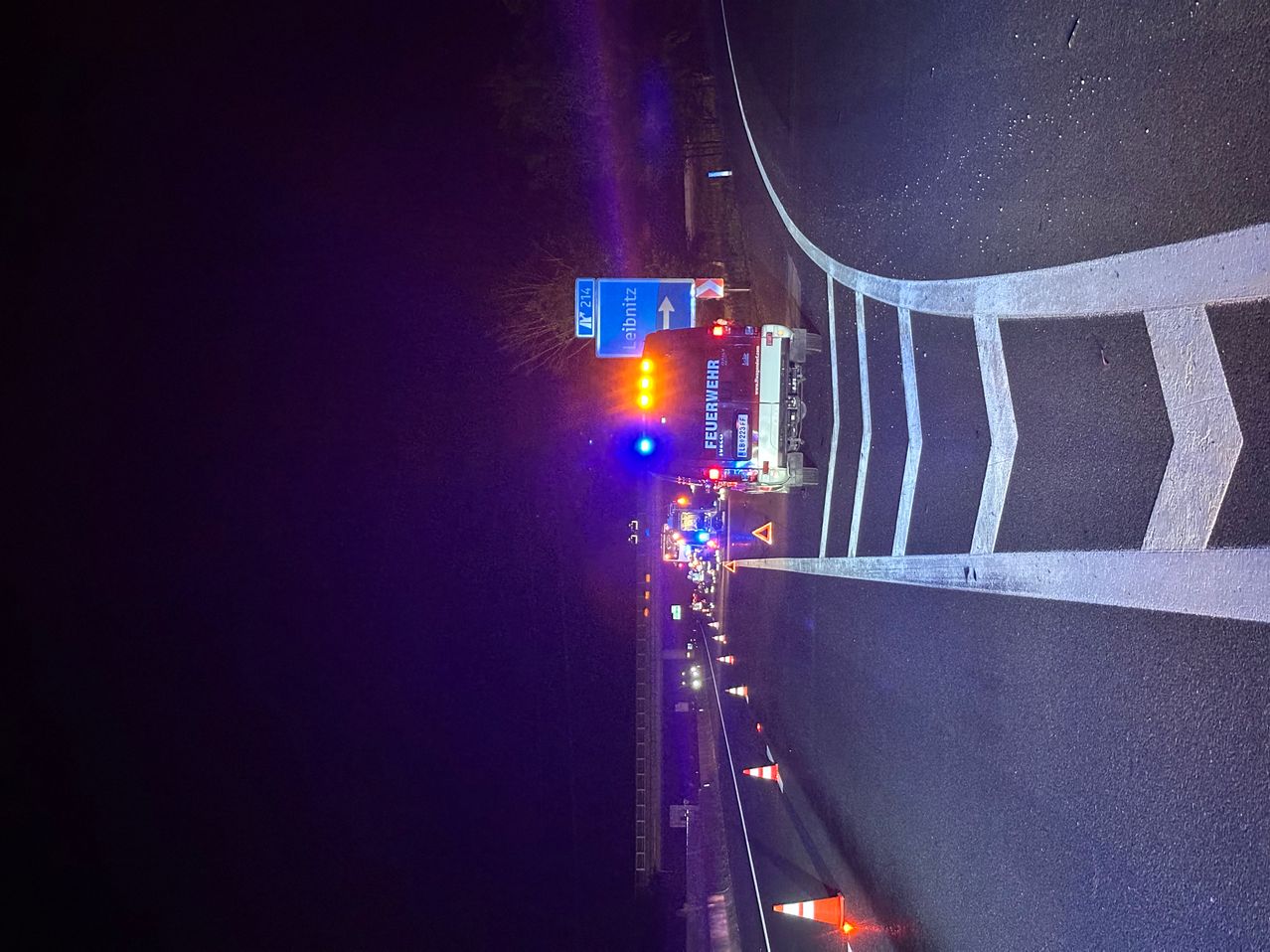 Ein Feuerwehrfahrzeug mit eingeschalteten Lichtern steht am Straßenrand, möglicherweise als Reaktion auf einen Vorfall.