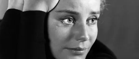 Ein Schwarz-Weiß-Foto zeigt eine Frau mit kurzen Haaren, die ein Rollkragenshirt trägt. Sie hat Tränen in den Augen und hält ihren Kopf mit beiden Händen.